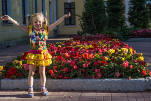Joyful child with arms raised beside colorful flowers, representing the joy and new life found in believing the gospel.