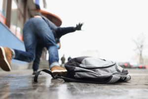 Person stumbling on a city sidewalk while a backpack falls to the ground, illustrating how people can stumble over the message of the gospel.